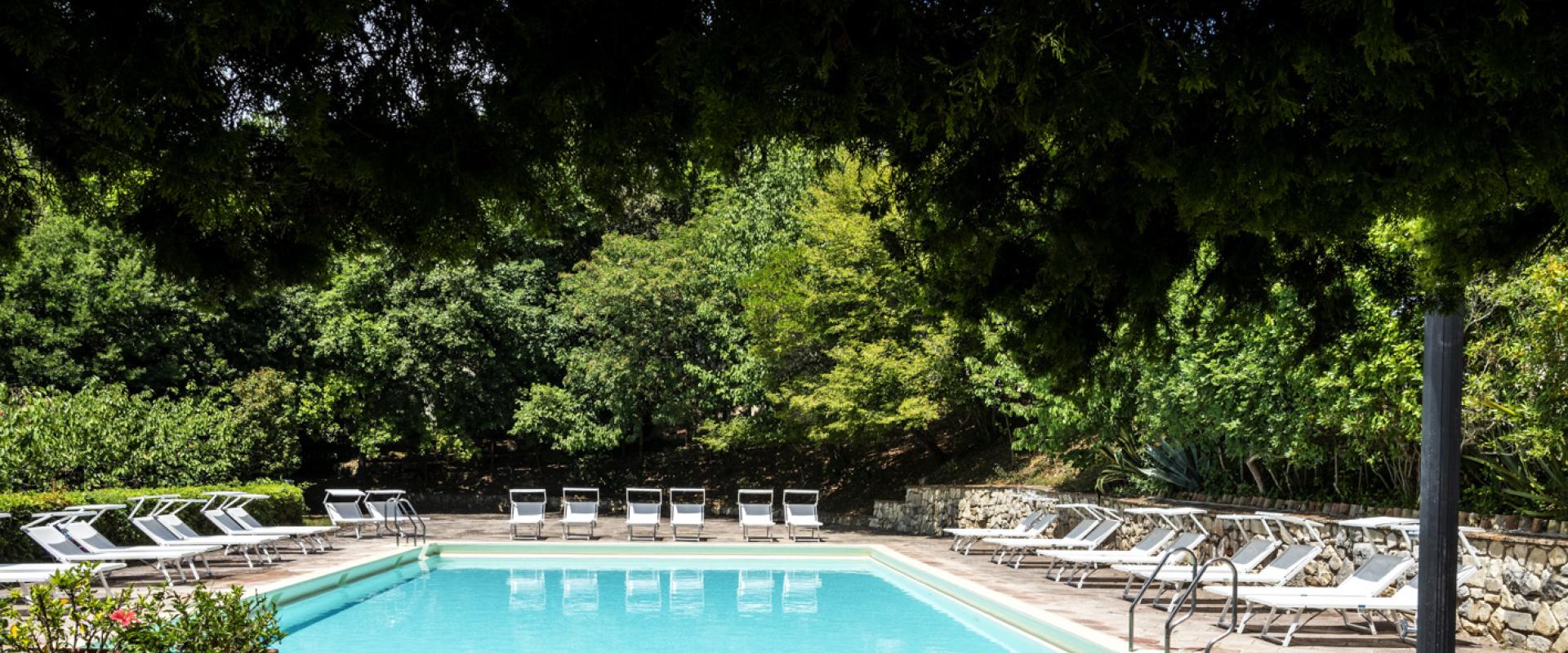 Piscina all'aperto con lettini, circondata da vegetazione lussureggiante.