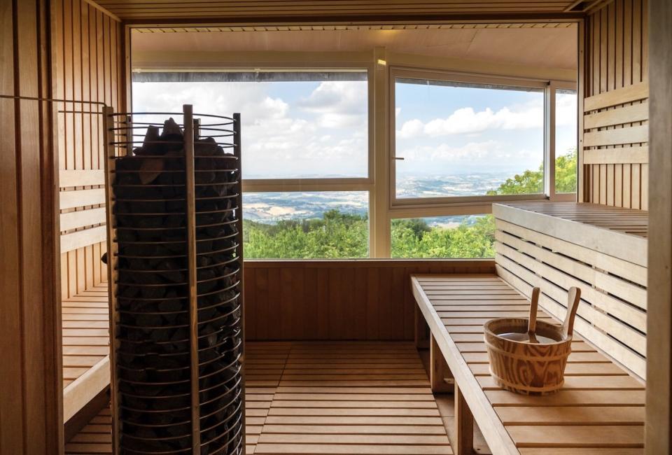 Sauna con vista panoramica sulle colline, interni in legno e secchio d'acqua.