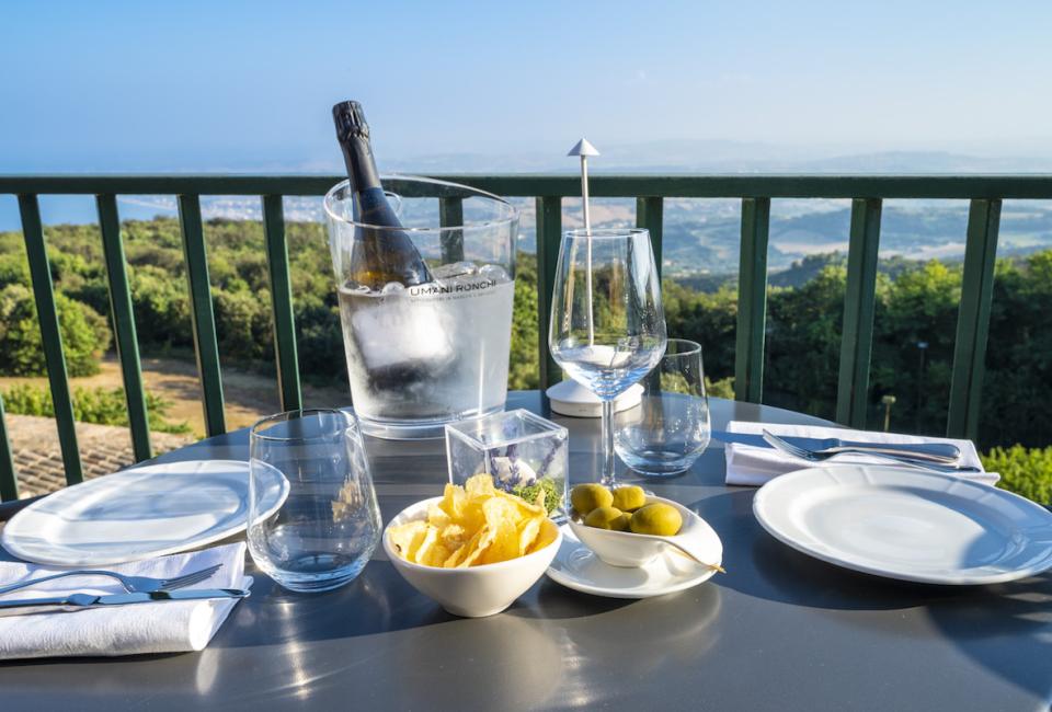 Tavolo apparecchiato con vista, spumante, patatine e olive.